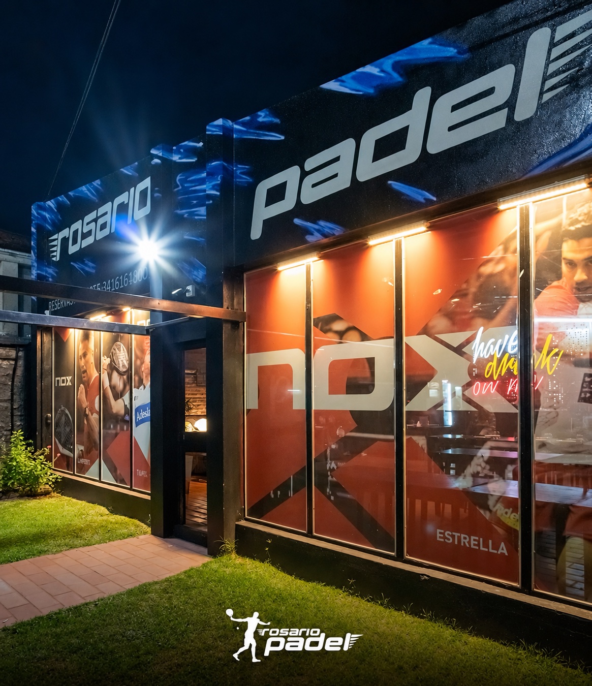 Entrada iluminada de Rosario Padel, con el cartel del club y su fachada vidriada