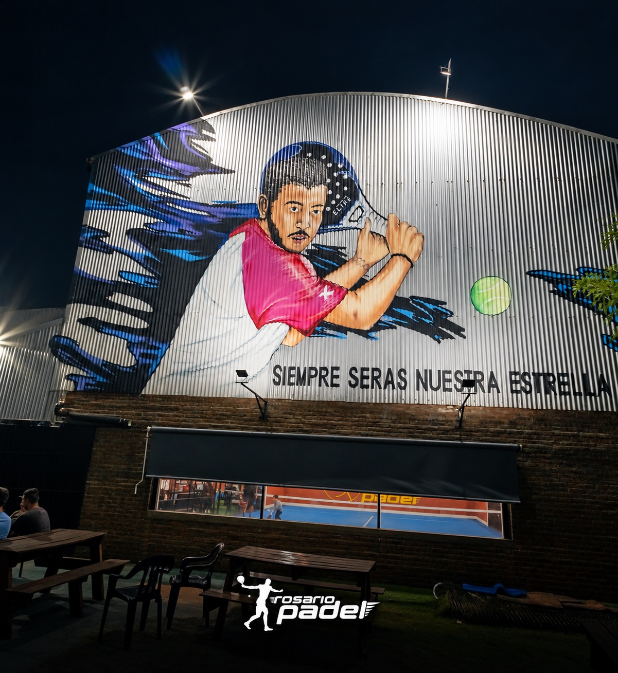 Frente del complejo de noche, con el mural del jugador y la marca Rosario Padel